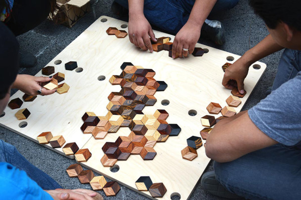 Vier Personen spielen das grid game auf dem Boden. Die Spielsteine befinden sich auf einem Holzbrett.